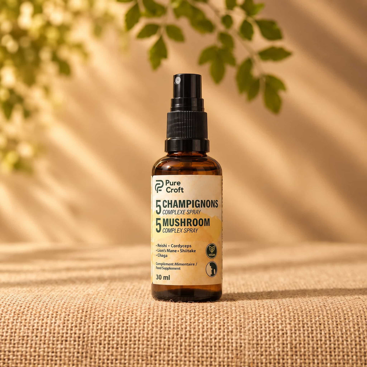 Un flacon unique de 30ml de Pure Croft Spray Complexe 5 Champignons avec un embout spray noir est centré sur un tapis en toile de jute. L'arrière-plan est un mur beige doux avec des reflets de lumière du soleil.