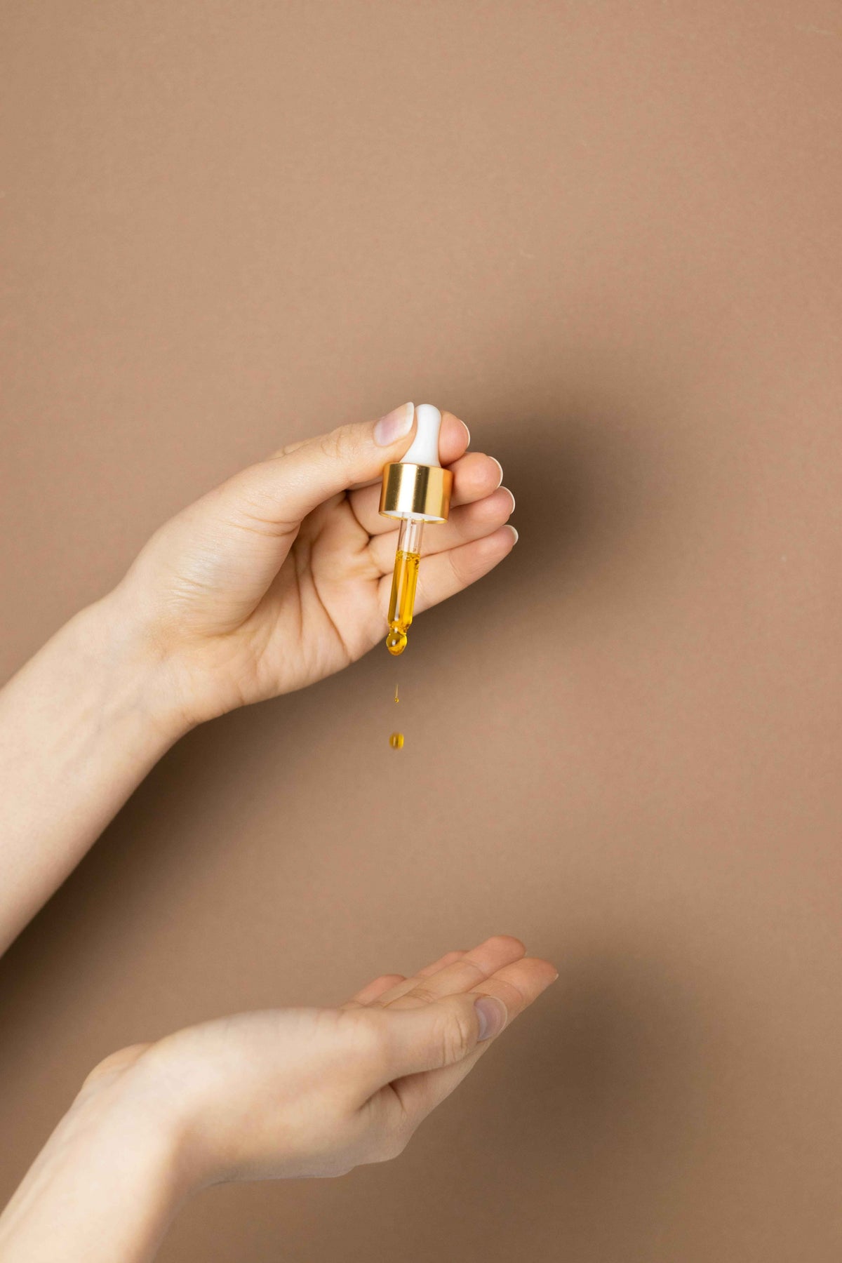 Golden functional mushroom serum drop from dropper into hand, luxury wellness product