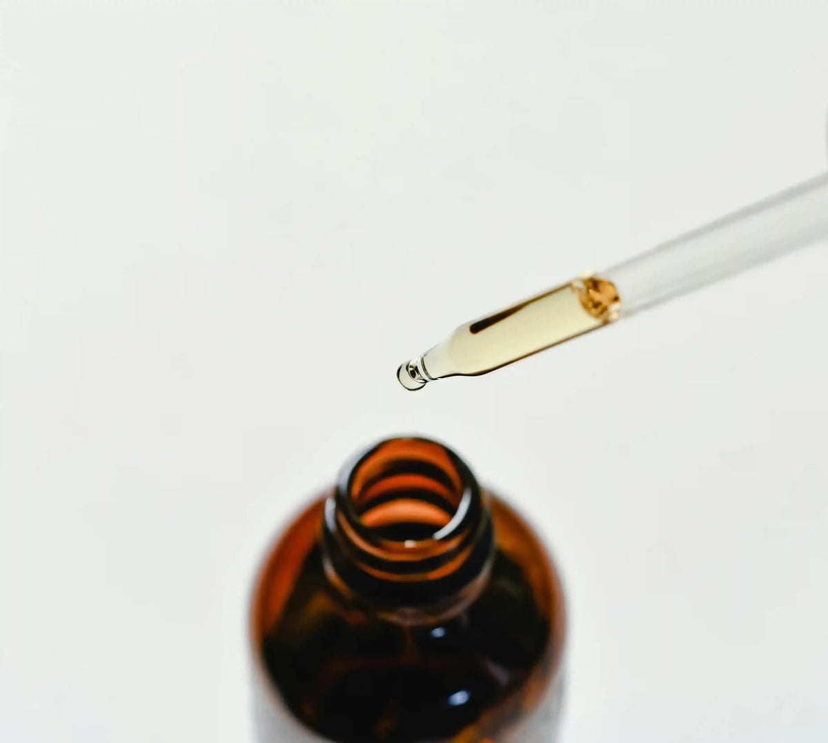 Dropper dispensing golden functional mushroom supplement oil from amber bottle