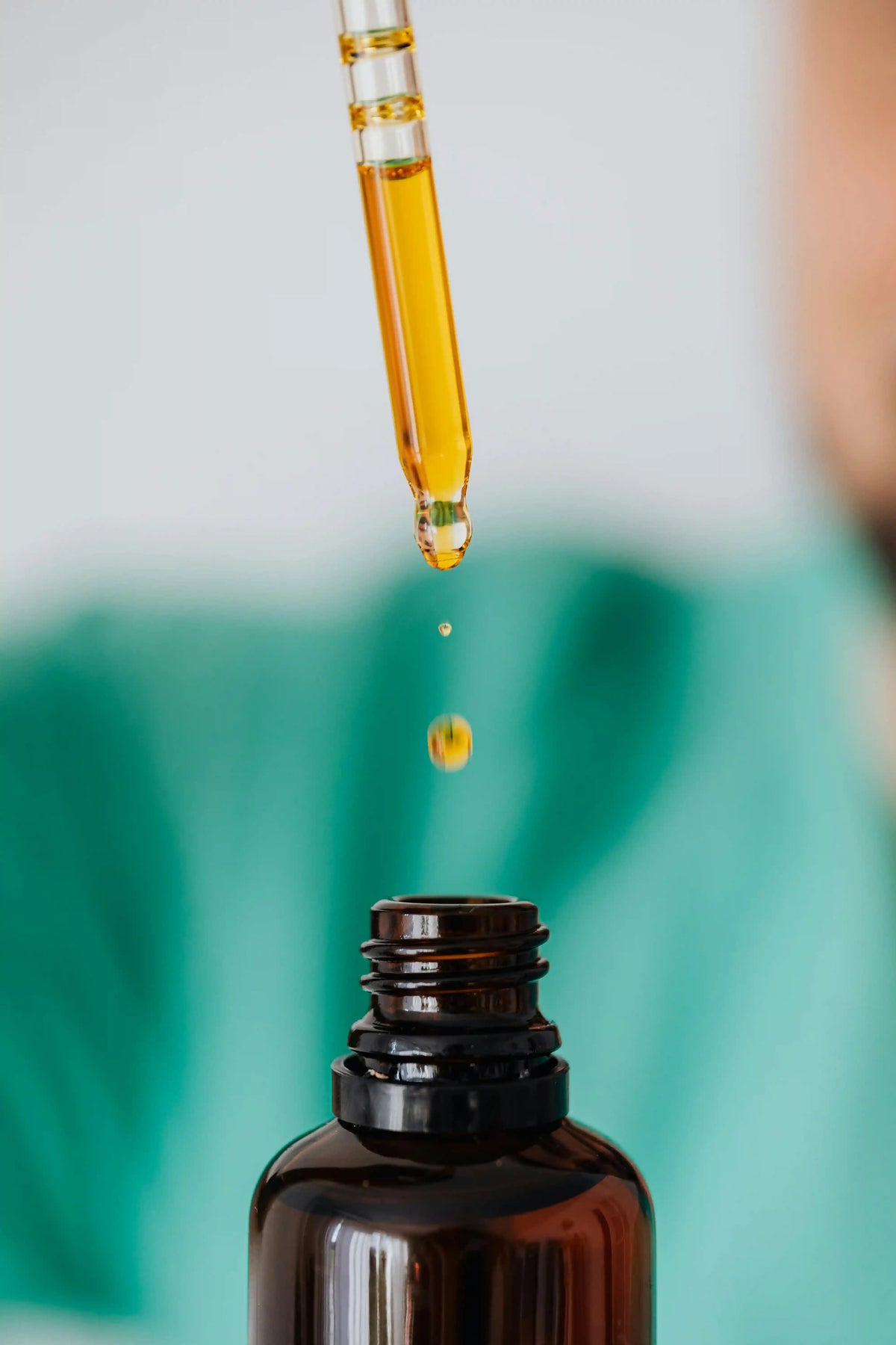 Golden functional mushroom oil droplet falling from dropper into amber bottle