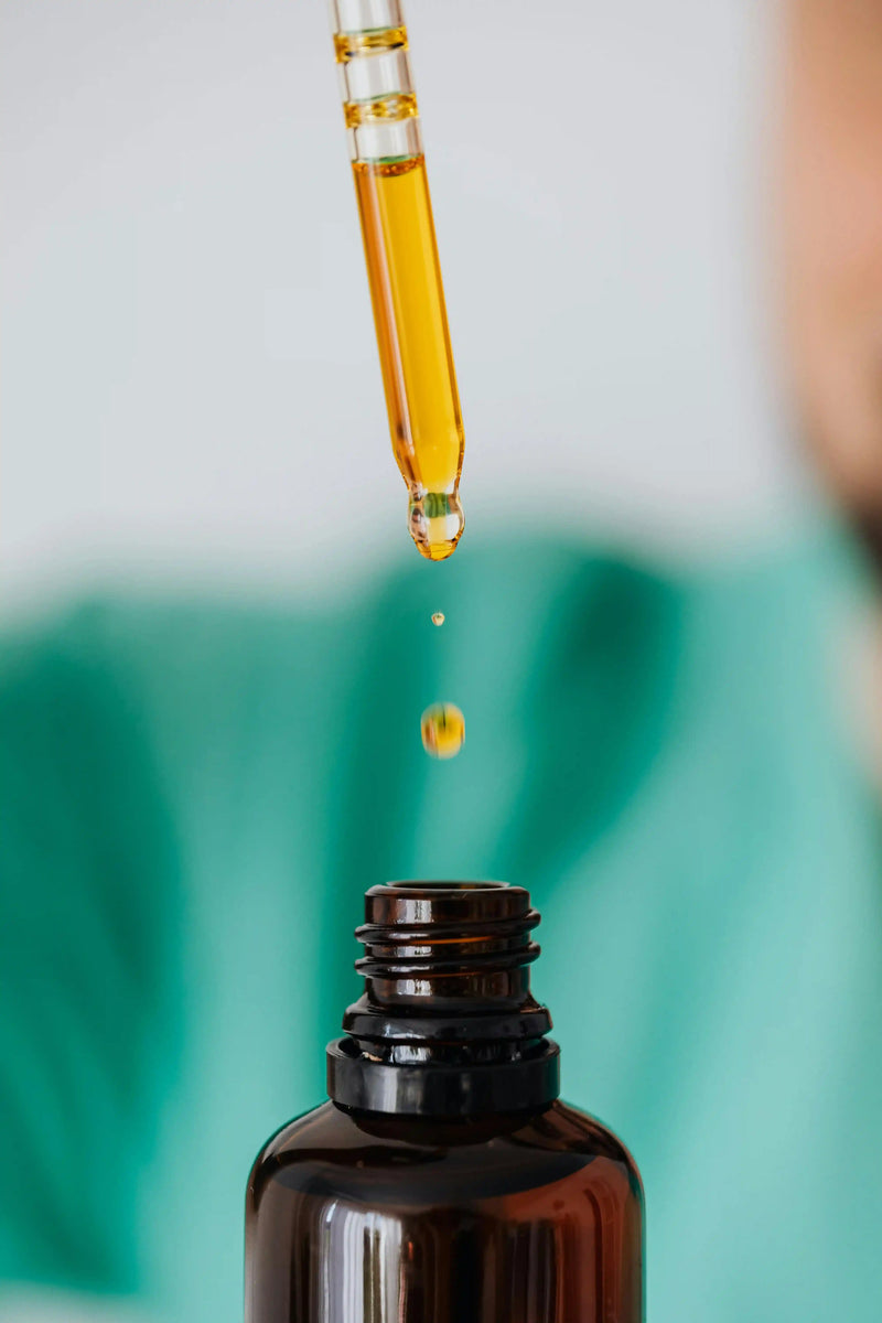 Golden functional mushroom oil droplet falling from dropper into amber bottle