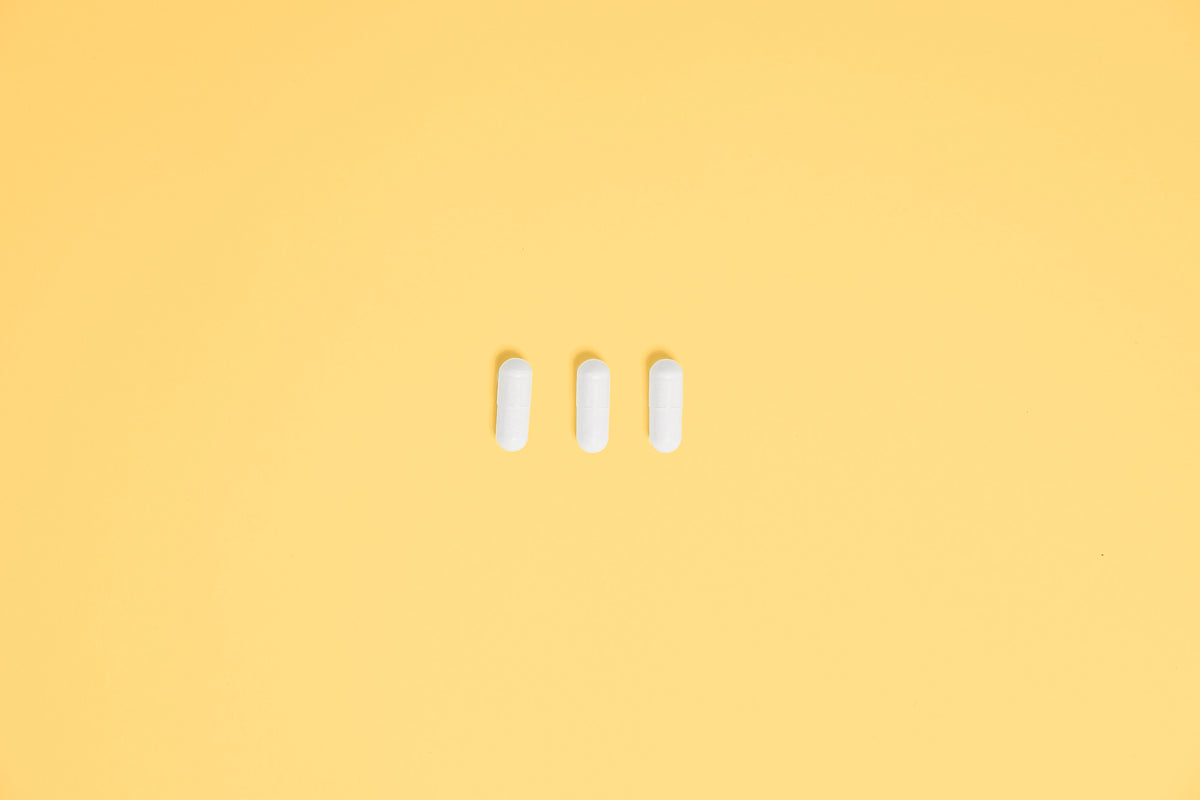 Three white functional mushroom supplement capsules on a yellow background